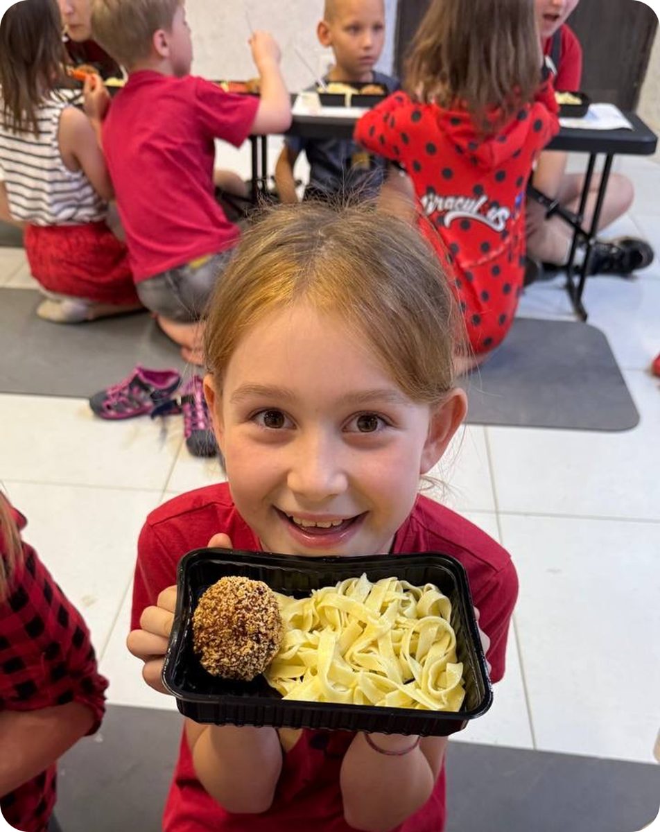 A smiling girl holds up her warm meal at the Mission 823 feeding program in Nikopol, Ukraine